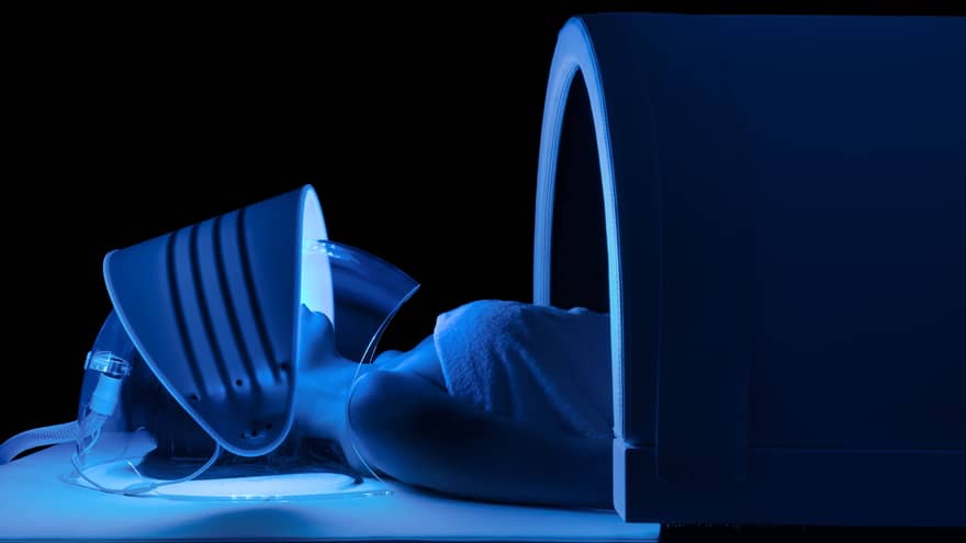 Person wears mask with blue lights under dome in dark spa room